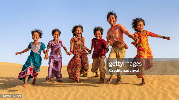 gruppe glücklicher indischer kinder, die über sanddüne laufen, indien - rajasthani youth stock-fotos und bilder