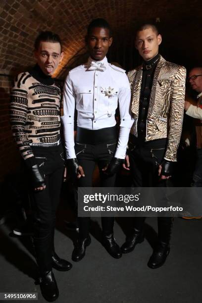 Backstage at the Julien Macdonald show during London Fashion Week Autumn/Winter 2016/17, three models wear tight black bondage style trousers, one...