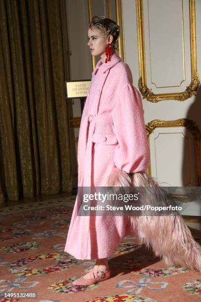 Backstage at the Simone Rocha show during London Fashion Week Autumn/Winter 2016/17, a model wears a double breasted belted coat in metallic pink...