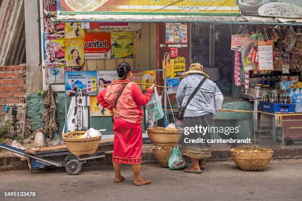 dos mujeres laosianas fuera de una tienda con palos de transporte - all people fotografías e imágenes de stock