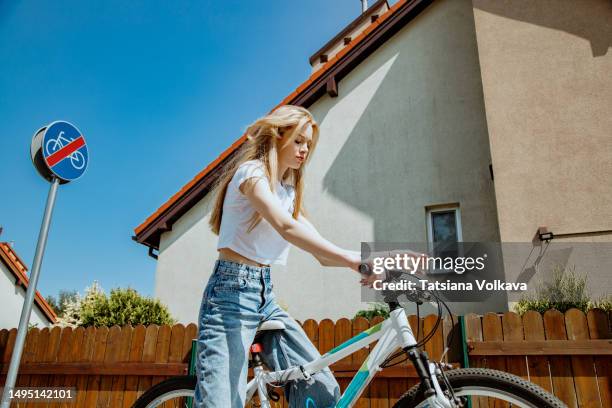 slim teenage girl riding bike near big beige house with road sign prohibiting cycling - dumb blonde stock pictures, royalty-free photos & images