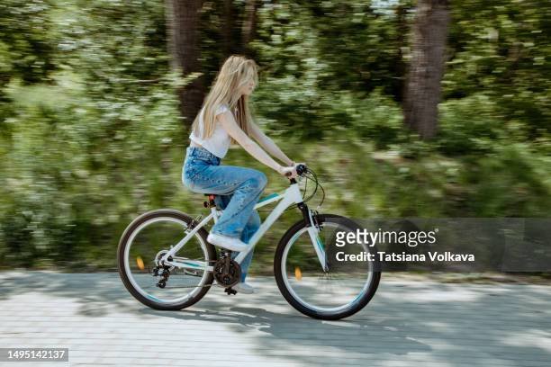 teenage girl with blond hair riding white bike on sidewalk passing by buses and trees - girl bike stock pictures, royalty-free photos & images
