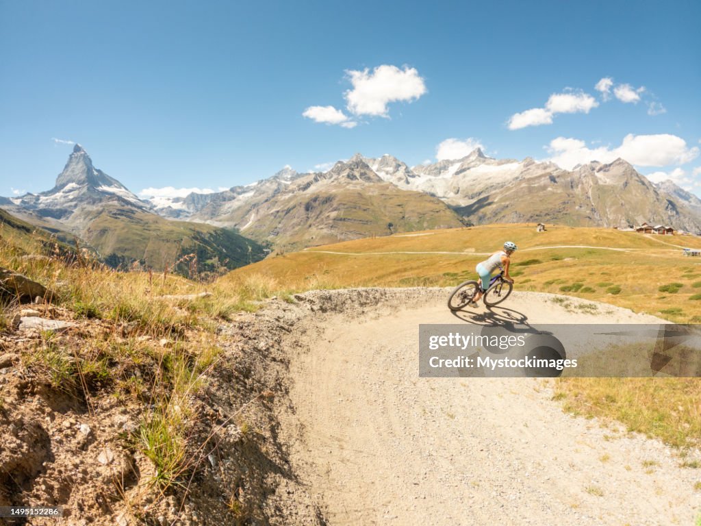 Female mountain biker on dirt trail, view of the famous Matterhorn mountain peak in distance, Switzerland