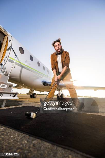 mann mit golfschläger vor privatjet macht albernes gesicht - men doing quirky things stock-fotos und bilder