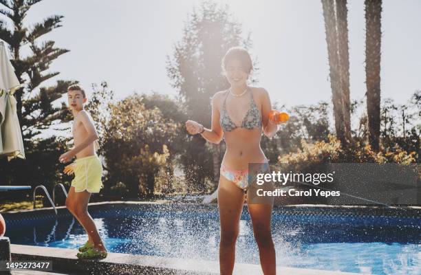 two friends have fun playing with water bombs poolside - kids pool games stock-fotos und bilder