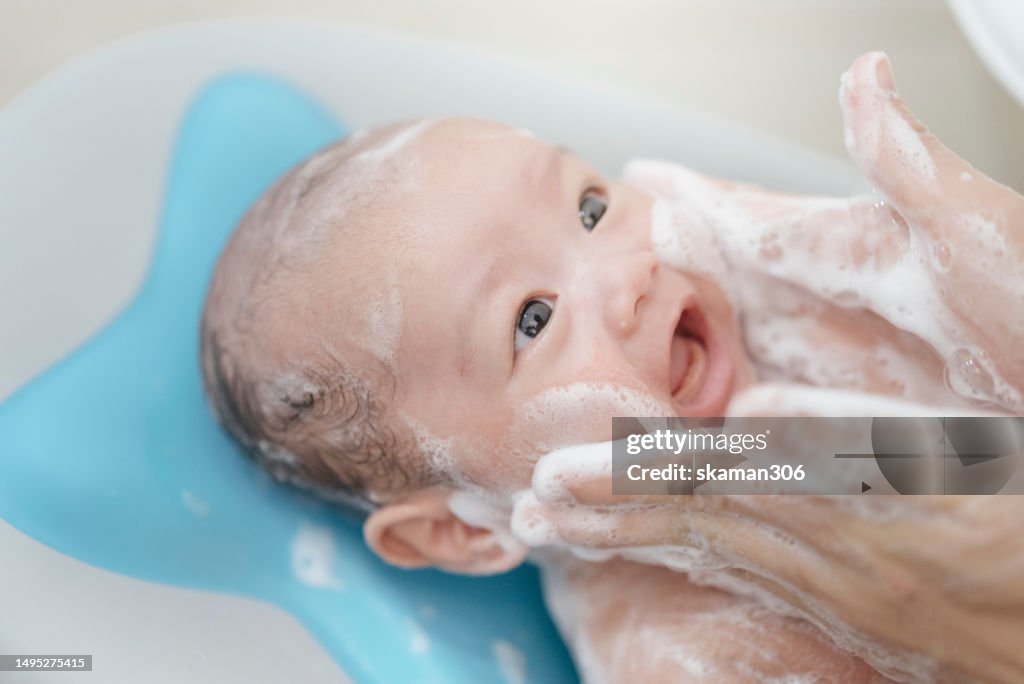 Asian baby leaning back on the baby bathtub and enjoy after mother shower and scrub bath foam Domestic life