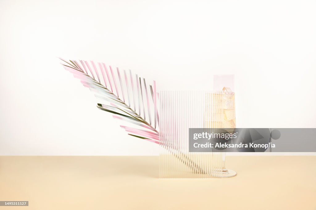 Still life composition - 3d stage with crystal champagne glass filled with white sparkling wine and pink colored dry palm leaf on on pastel cream beige and white background with copy space.