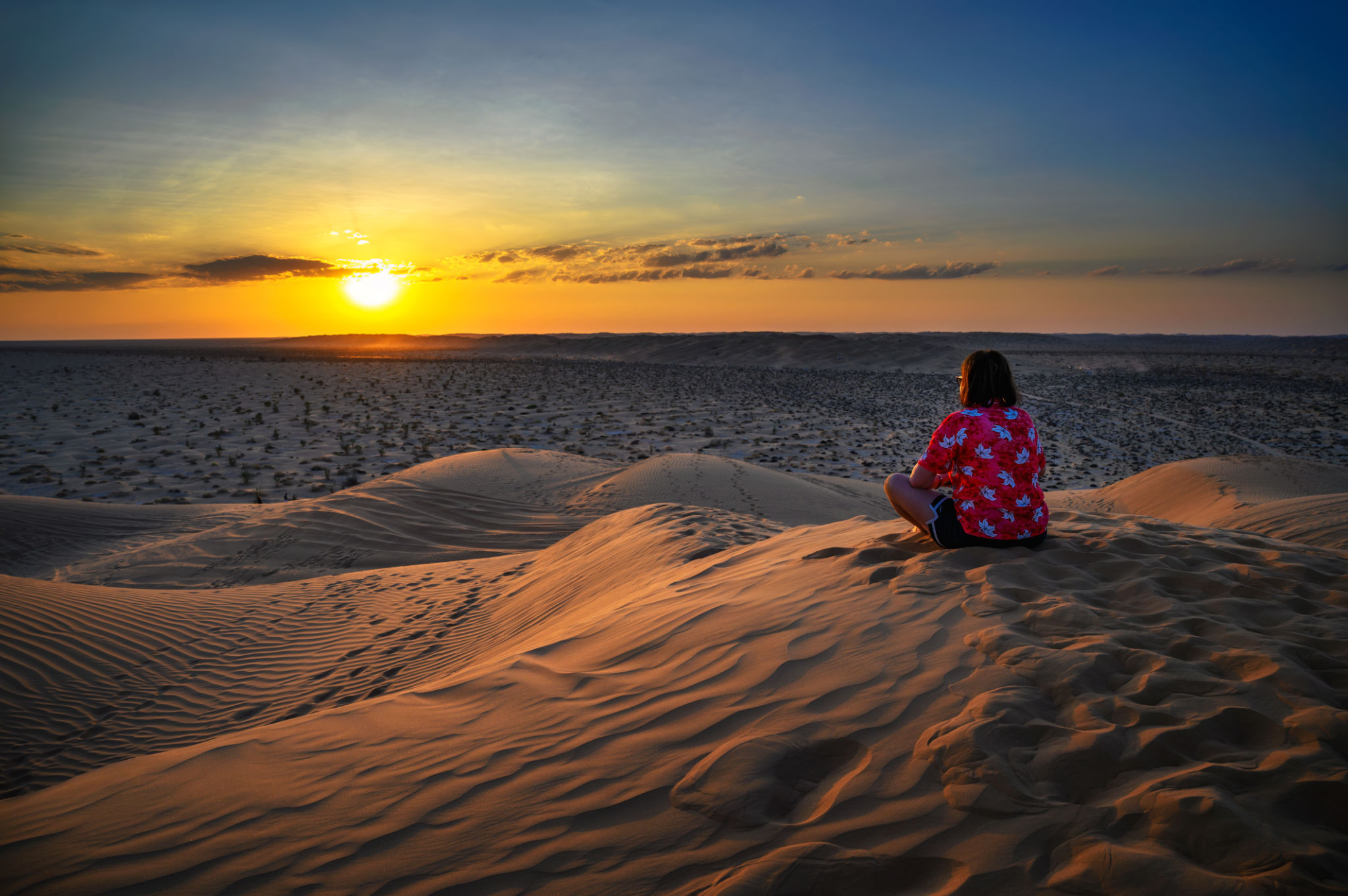 Woman watching a sunset over the sand dunes of the Arabian Desert in Oman Woman watching a sunset over the sand dunes of the Arabian Desert in Oman