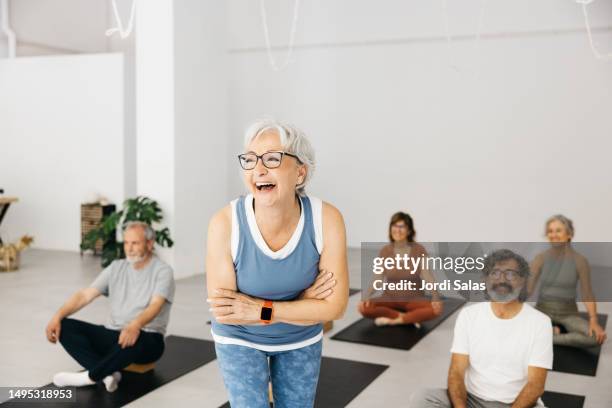 portrait of a senior woman laughing in a yoga studio with her class - senior yoga stock-fotos und bilder
