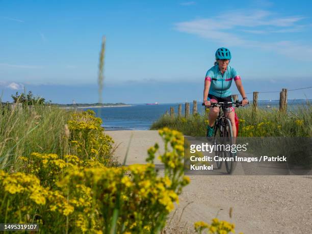 woman riding bike on dirt track near sea - bicycle flowers stock pictures, royalty-free photos & images