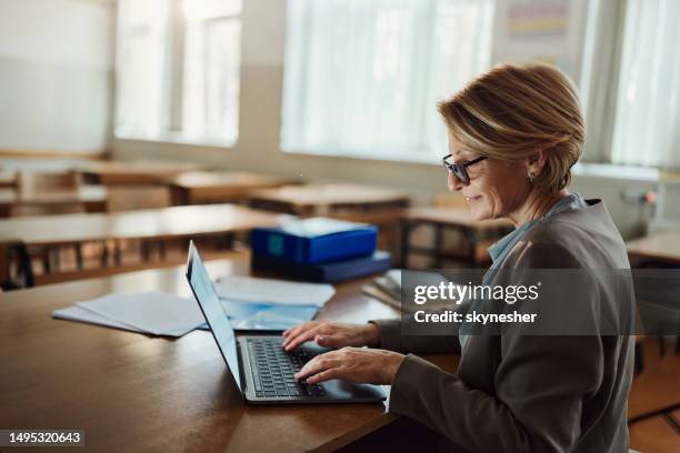 smiling female teacher working on laptop in the classroom. - trainer stock pictures, royalty-free photos & images