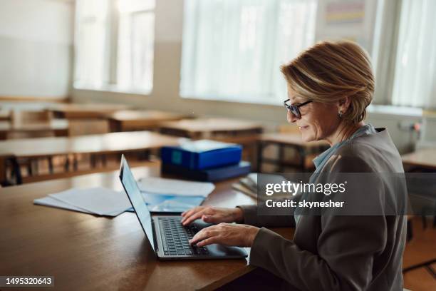 professora sorridente trabalhando em laptop na sala de aula. - professor de faculdade - fotografias e filmes do acervo