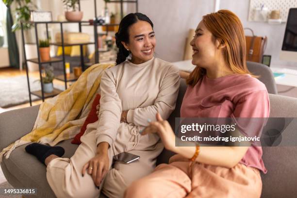 two women talking on a sofa in a living room - burmese people stock pictures, royalty-free photos & images