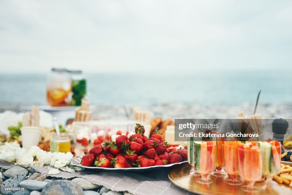 Summer picnic outdoors on a sunny day with croissants, strawberries, grapes, cheese, carrots, cucumbers. Vegetarian snack in nature.