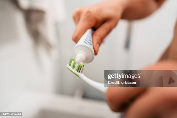 joven poniéndose pasta de dientes para cepillarse los dientes en el baño - dientes humanos fotografías e imágenes de stock