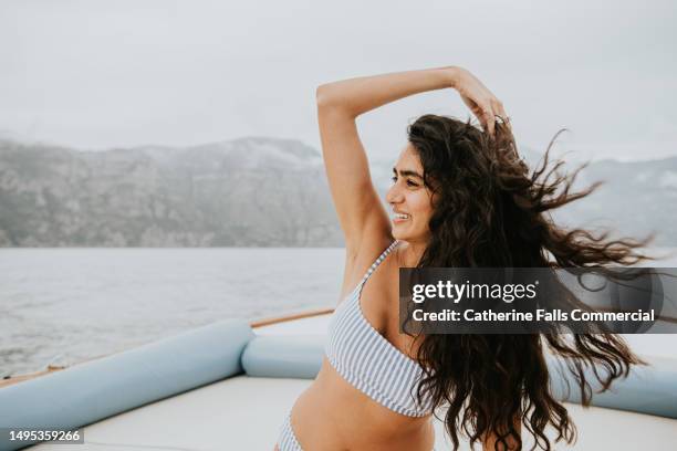 a beautiful young woman on a boat, runs her fingers through her long windswept hair - hair conditioner stockfoto's en -beelden