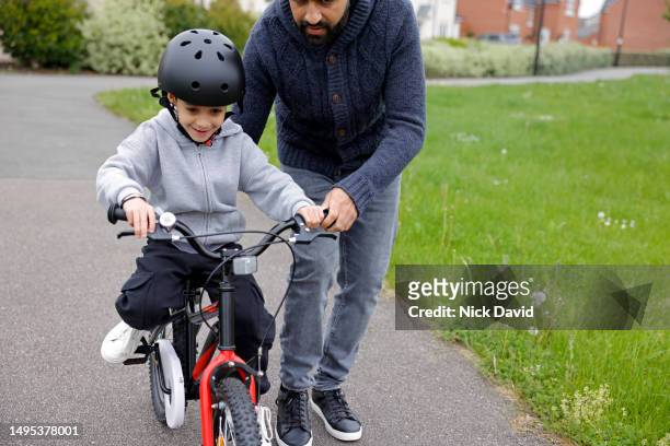 a young boy learning to ride a bike with his dad - single father stock pictures, royalty-free photos & images