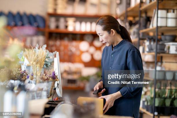 quality over speed and market wisely to improve your customer retention. side view of a japanese flower shop owner working inside a cashier counter and using a barcode reader to scan artificial flowers into a point-of-sale system (pos). - point stock photos et images de collection