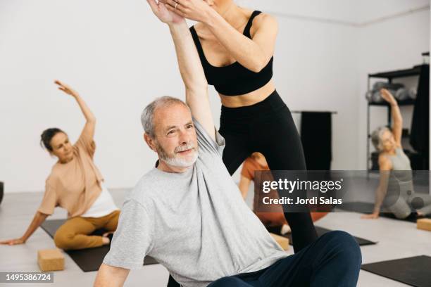 yoga instructor teaching a senior man the a pose in a yoga class - pensioners demonstrate in barcelona stock pictures, royalty-free photos & images