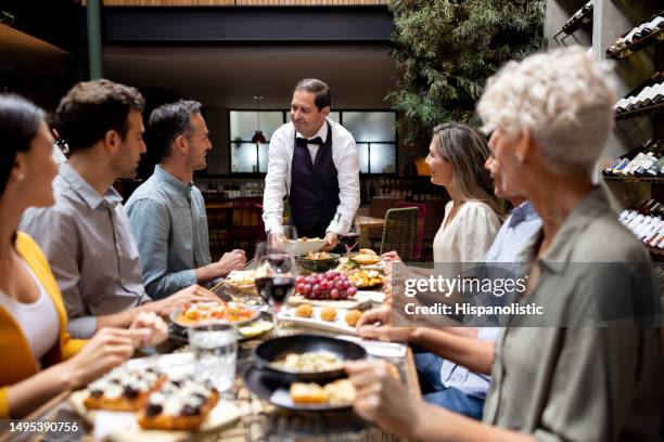 kellner, der einer gruppe von freunden in einem restaurant essen serviert - weinbar stock-fotos und bilder