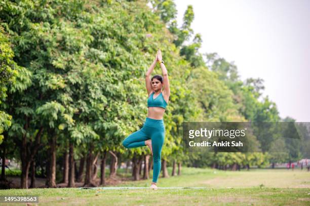 young woman performing yoga asana or meditation in tree position or vrikshasana - tree position stock pictures, royalty-free photos & images