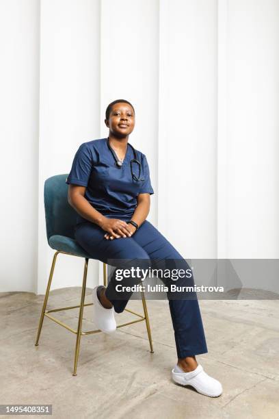 good-looking black female paramedic in blue hospital gown sitting on chair - showus doctor stock pictures, royalty-free photos & images