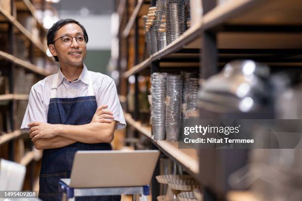 using order and inventory management software to improve all process in the small business. portrait of a male japanese store owner working in a storehouse of home decor products to track stock levels for support customer orders. - asien e commerce stock-fotos und bilder