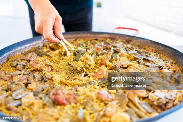 close-up of high angle view of the hand of a man serving a delicious basque style meat paella from a casserole outdoors - paella alicante stock pictures, royalty-free photos & images