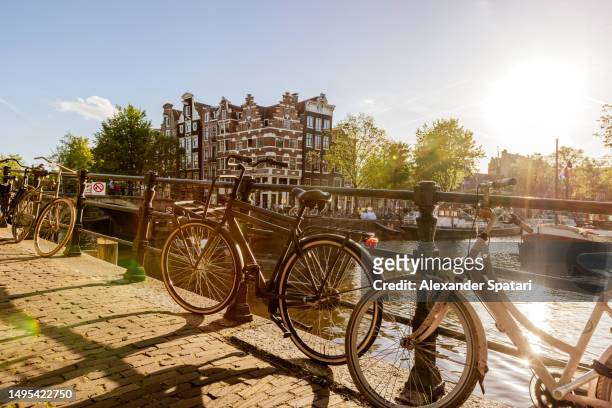 sun shining through bikes by the canal on a sunny summer day, amsterdam, netherlands - amstel stockfoto's en -beelden