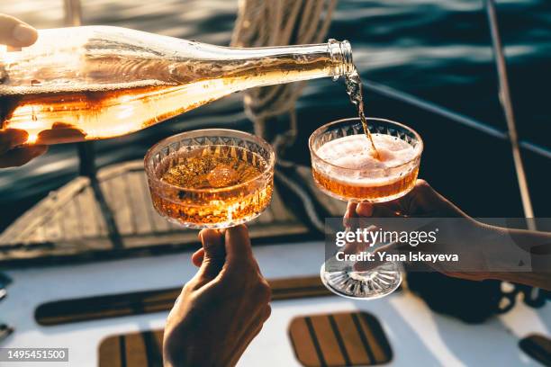 a close-up shot of friends clinking sparkling wine glasses at sunset on a yacht - fizz stock pictures, royalty-free photos & images