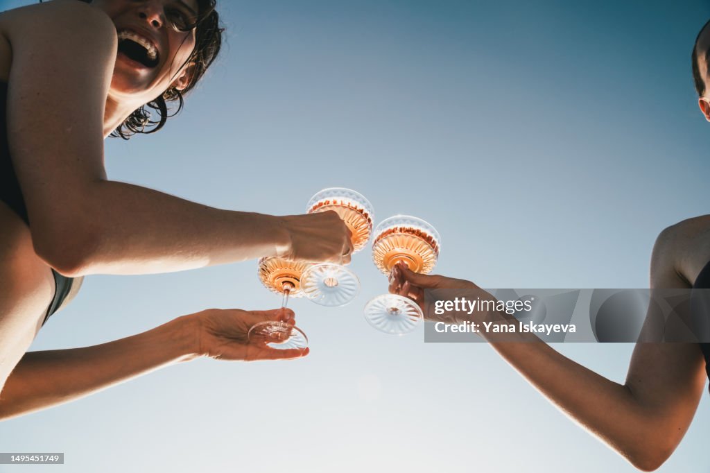 A close-up shot of friends clinking sparkling wine glasses at sunset on a yacht