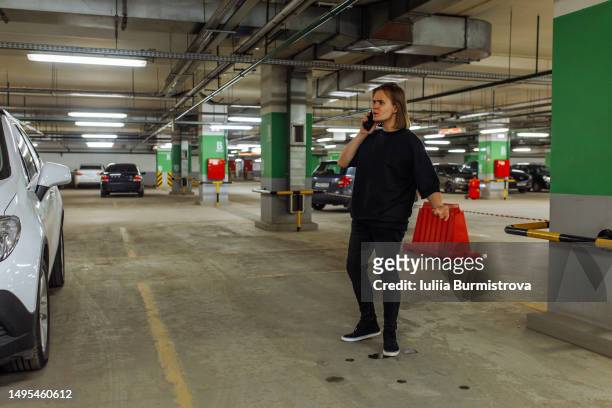 frustrated young man calling to police standing on empty parking lot in underground garage - fagotto foto e immagini stock