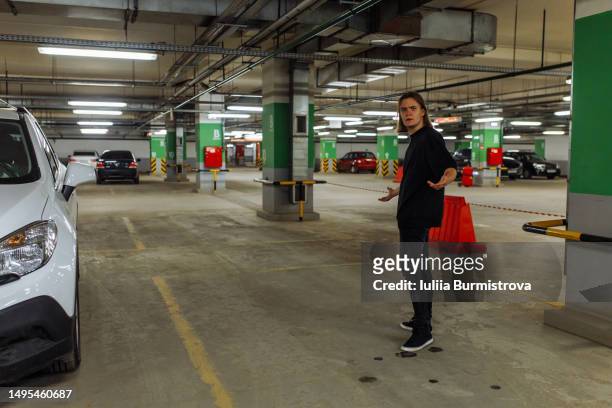 frustrated young man standing on empty parking lot looking for absent car in underground parking garage - fagotto foto e immagini stock