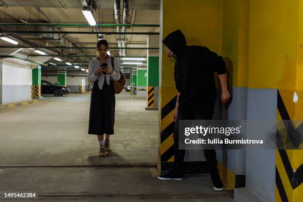 unsuspicious teenage girl walking in underground parking lot using smart phone while male stalker waiting to attack - mugger stock pictures, royalty-free photos & images