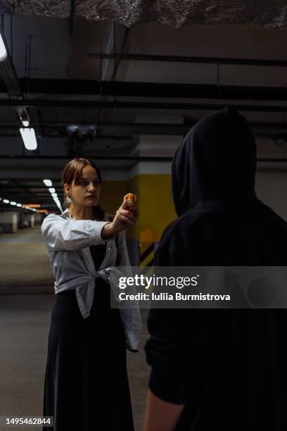 fearful teenage girl holding pepper spray to defend from male stalker in underground parking garage - mugger stock pictures, royalty-free photos & images