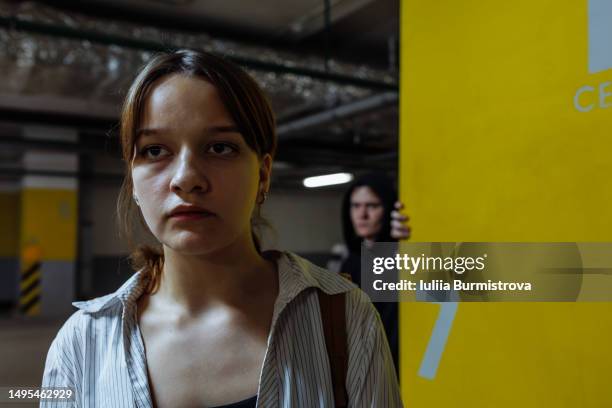 worried teenage girl walking in underground garage followed by man peeking over corner behind - stalking photos et images de collection