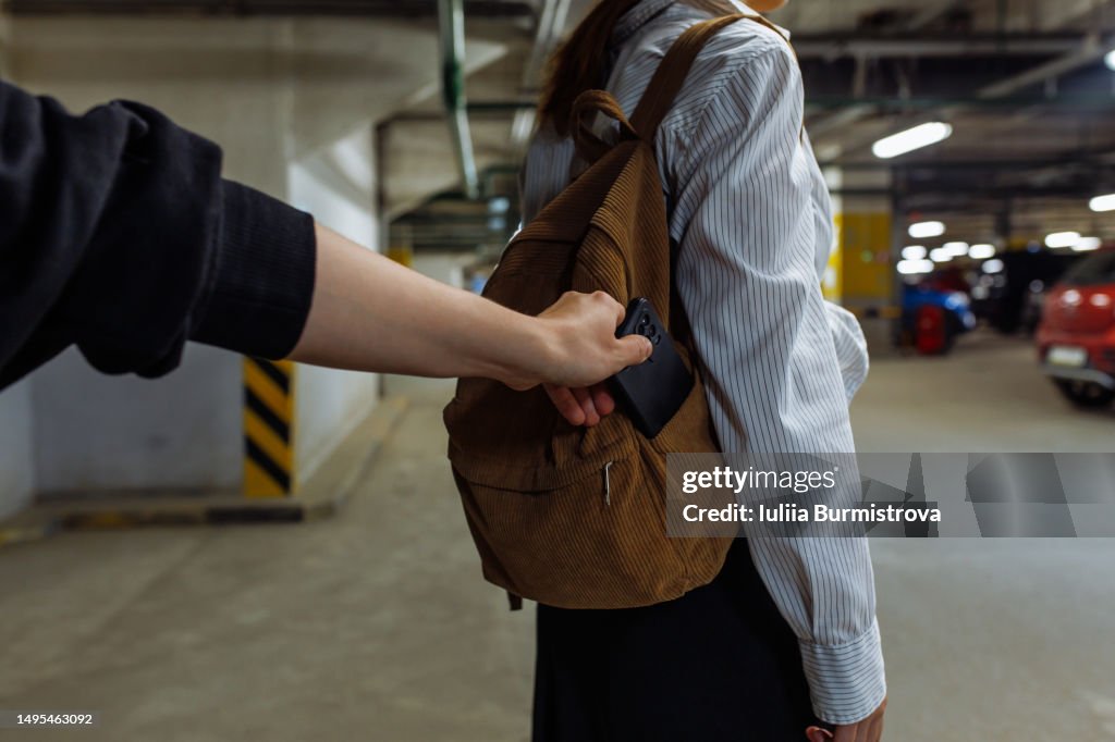 Hand of unrecognizable criminal taking mobile phone from backpack of unsuspicious female teenager