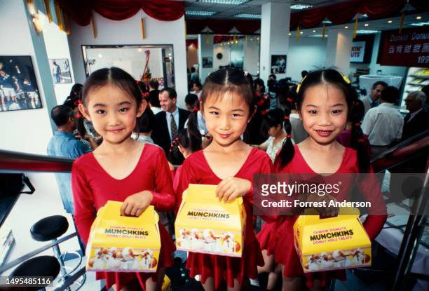 Portrait of three young girls as they hold carboard boxes of 'Munchkins' during the opening of Dunkin' Donuts shop, Beijing, China, 1990s.