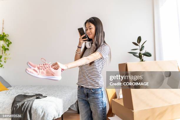 young asian woman capturing photos of pre-owned sneakers for online resale. exploring the concept of second-hand buying and selling through the internet or a mobile application - capturar una imagen fotografías e imágenes de stock