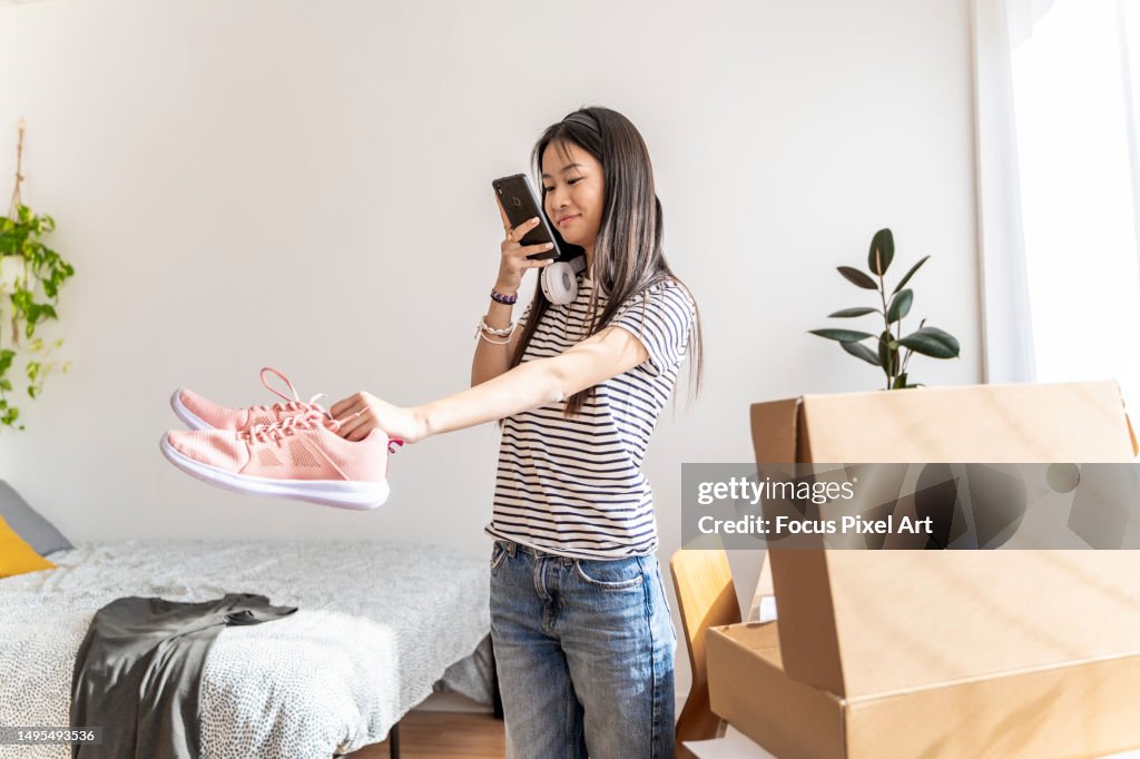 Young Asian woman capturing photos of pre-owned sneakers for online resale. Exploring the concept of second-hand buying and selling through the internet or a mobile application