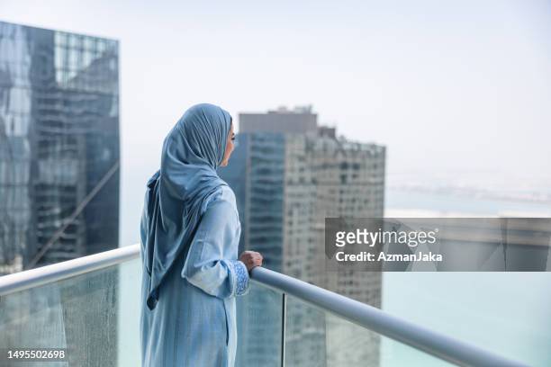 mature middle eastern women enjoys view of dubai from balcony - emirati woman stock pictures, royalty-free photos & images