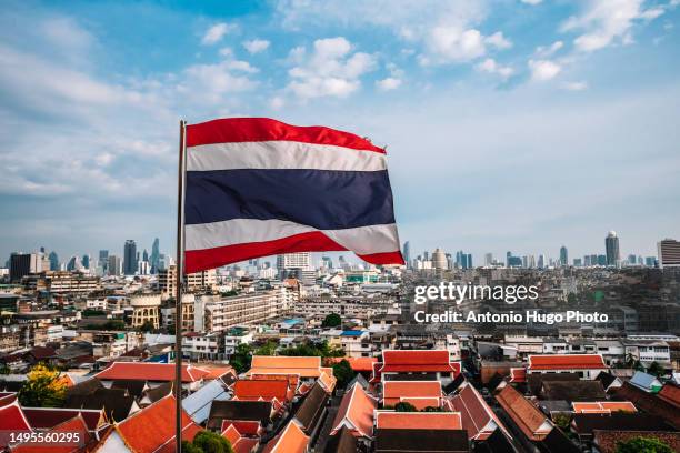flag of thailand flying. bangkok city in the background. - thailändische kultur stock-fotos und bilder