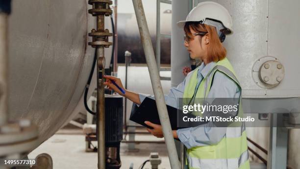 young asian female industrial engineer in hard hats checking steam boiler in chemical manufacturing factory. heavy industry and engineers. - air quality stock pictures, royalty-free photos & images