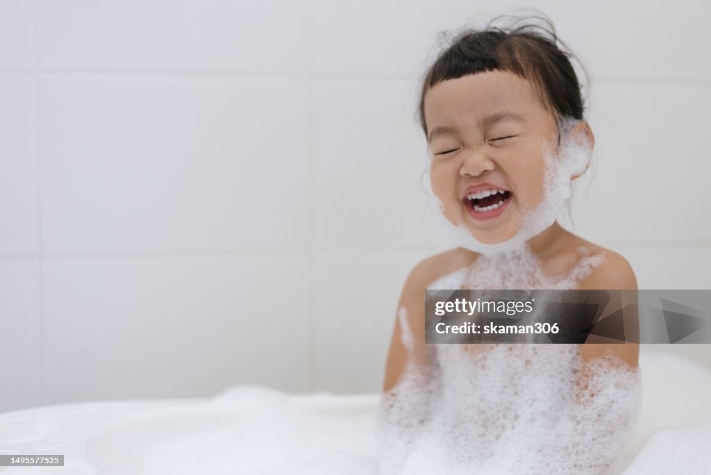Positive emotion Asian baby girls enjoy showering and playing foam and soap sud in bathroom copy space