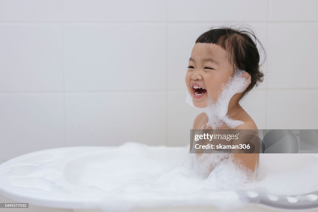 Positive emotion Asian baby girls enjoy showering and playing foam and soap sud in bathroom copy space