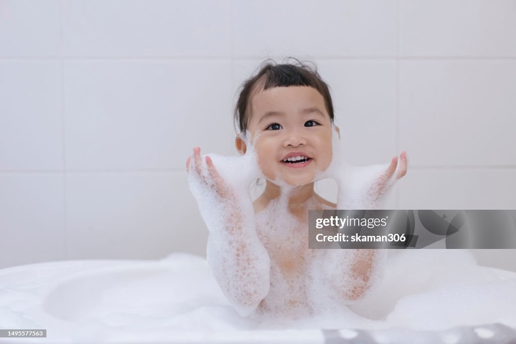 Positive emotion Asian baby girls enjoy showering and playing foam and soap sud in bathroom copy space