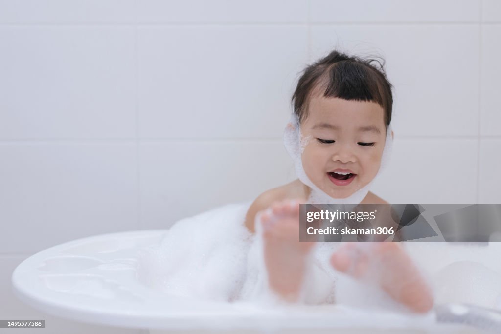 Facial expression Asian baby girl enjoy cleaning and shower foam inside bath tube copyspace