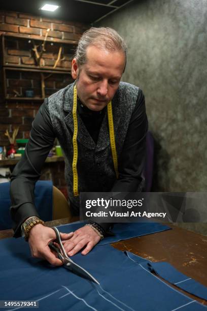 fashion designer is cutting cloth fabric on the table clippers are in men hand measure is on neck focus on foreground indoor vertical still - custom tailored suit stock pictures, royalty-free photos & images