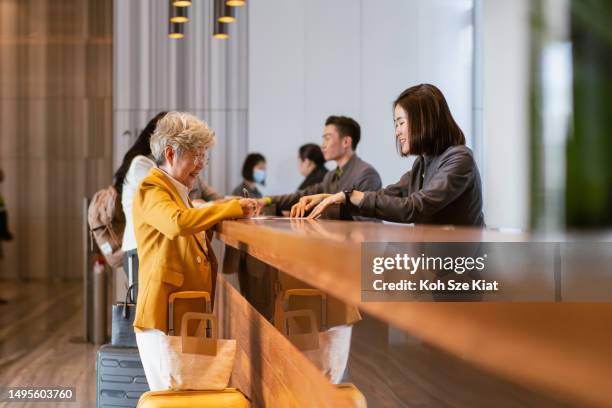 business travel - senior asian businesswoman checking into a hotel - star style lounge imagens e fotografias de stock