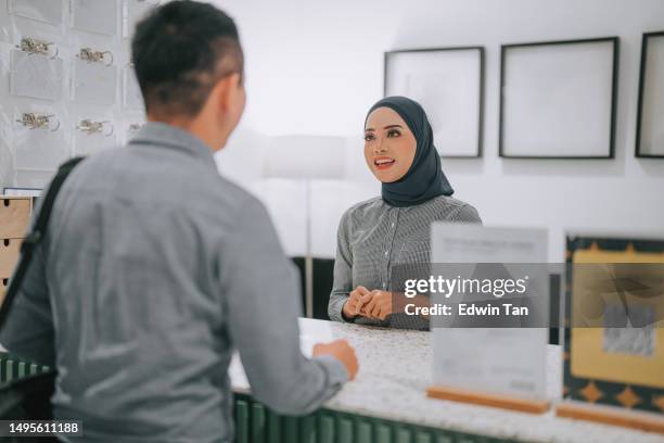 asian malay female receptionist greeting to customer at lobby reception desk - hotel reopening stock pictures, royalty-free photos & images